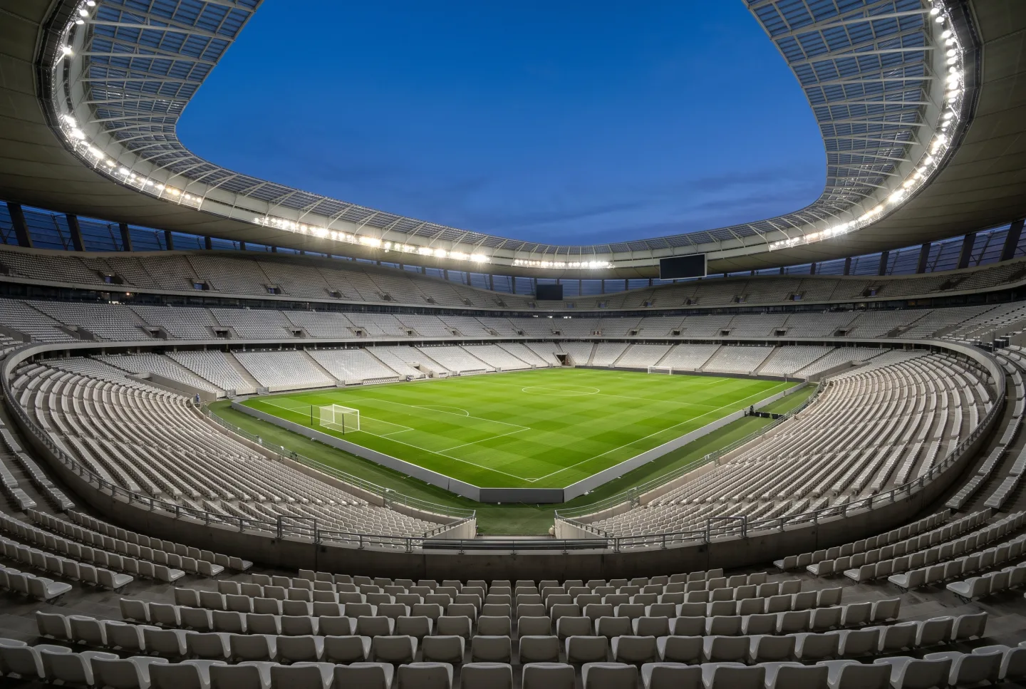 An empty modern football stadium at dusk with the floodlights on