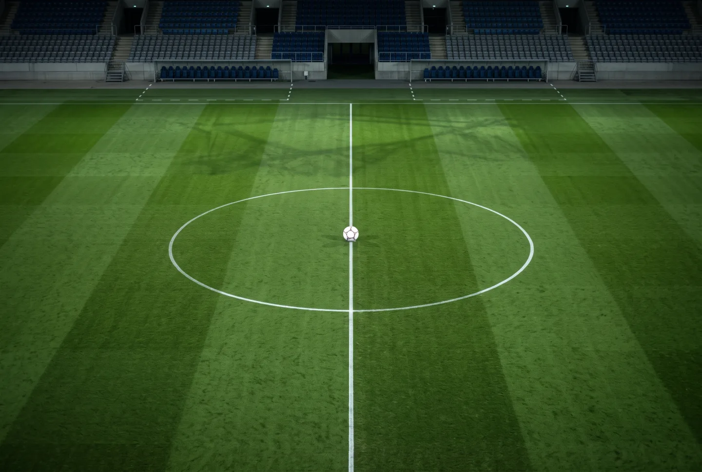 A single football on the centre spot of an empty floodlit pitch at night