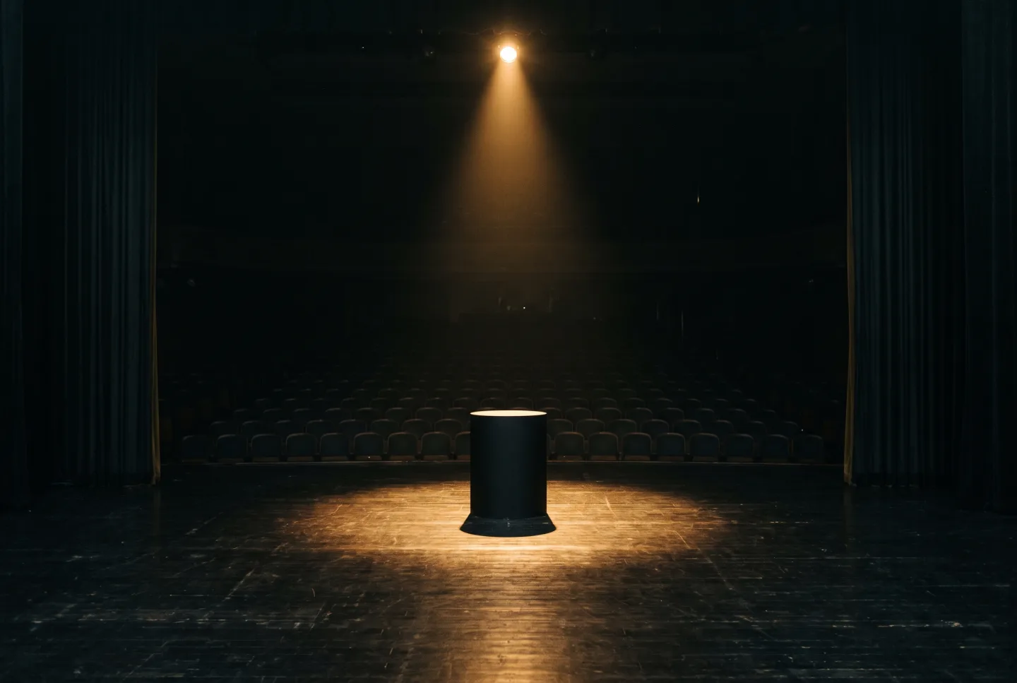 A bare plinth on an awards stage lit by a single overhead spotlight