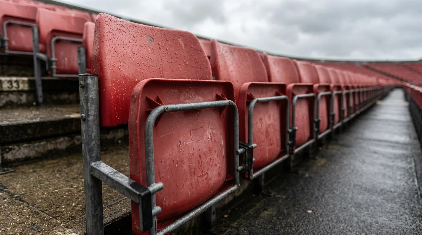 Rows of weathered red stadium seats beaded with raindrops in an empty stand