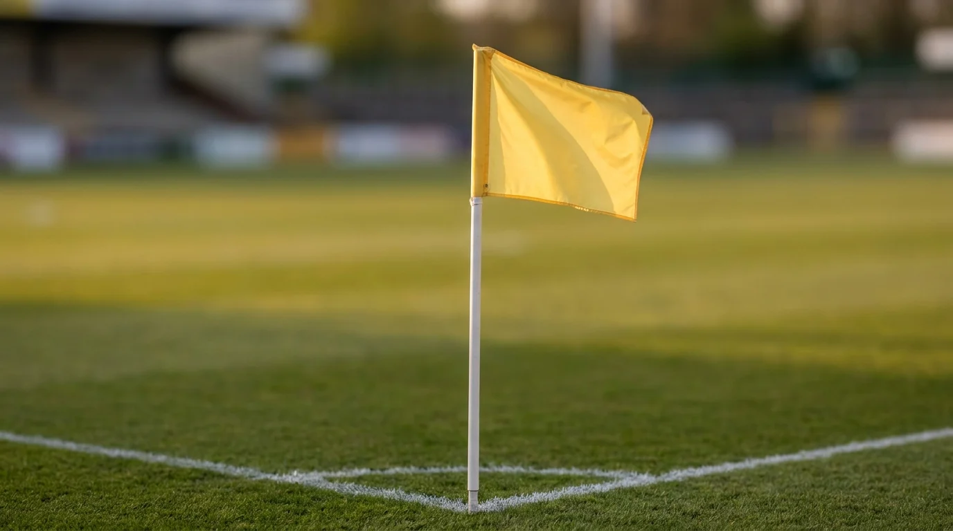 Yellow corner flag on a slim white pole at the corner of an empty sunlit football pitch