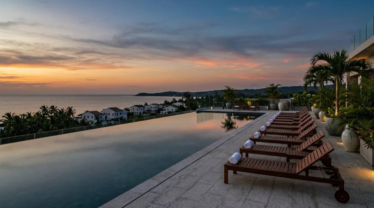 A luxury hotel rooftop infinity pool at dusk overlooking a quiet coastline