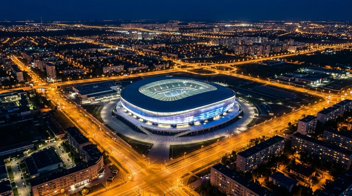 Aerial view of a large modern football stadium lit up at night surrounded by city lights