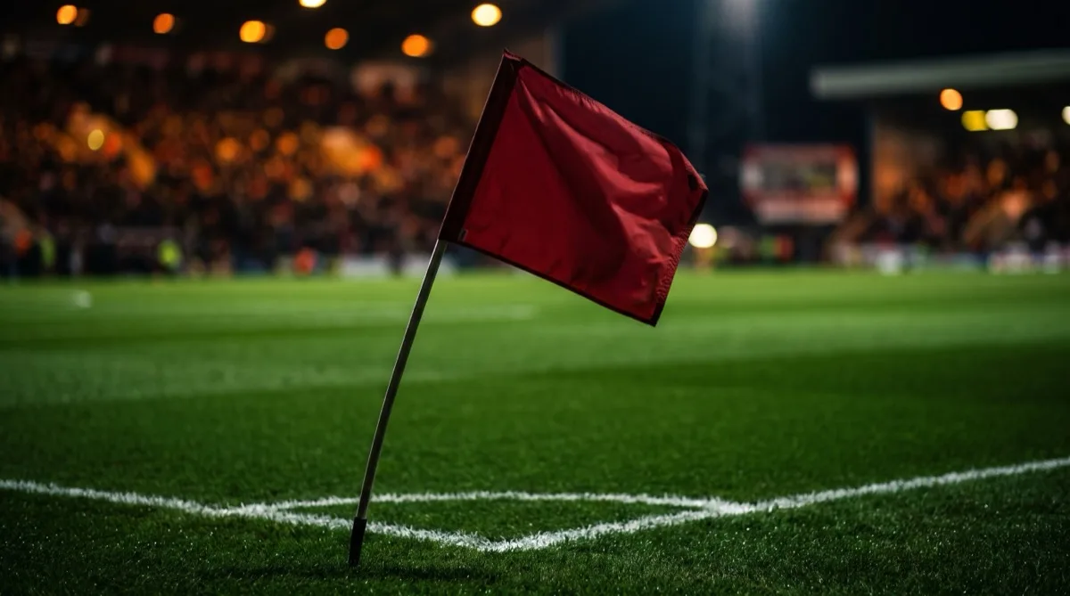 A corner flag on a floodlit football pitch at night with the crowd blurred behind