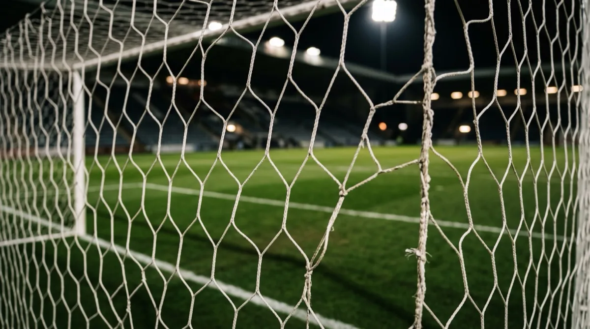 A view through a football goal net onto a floodlit pitch at night