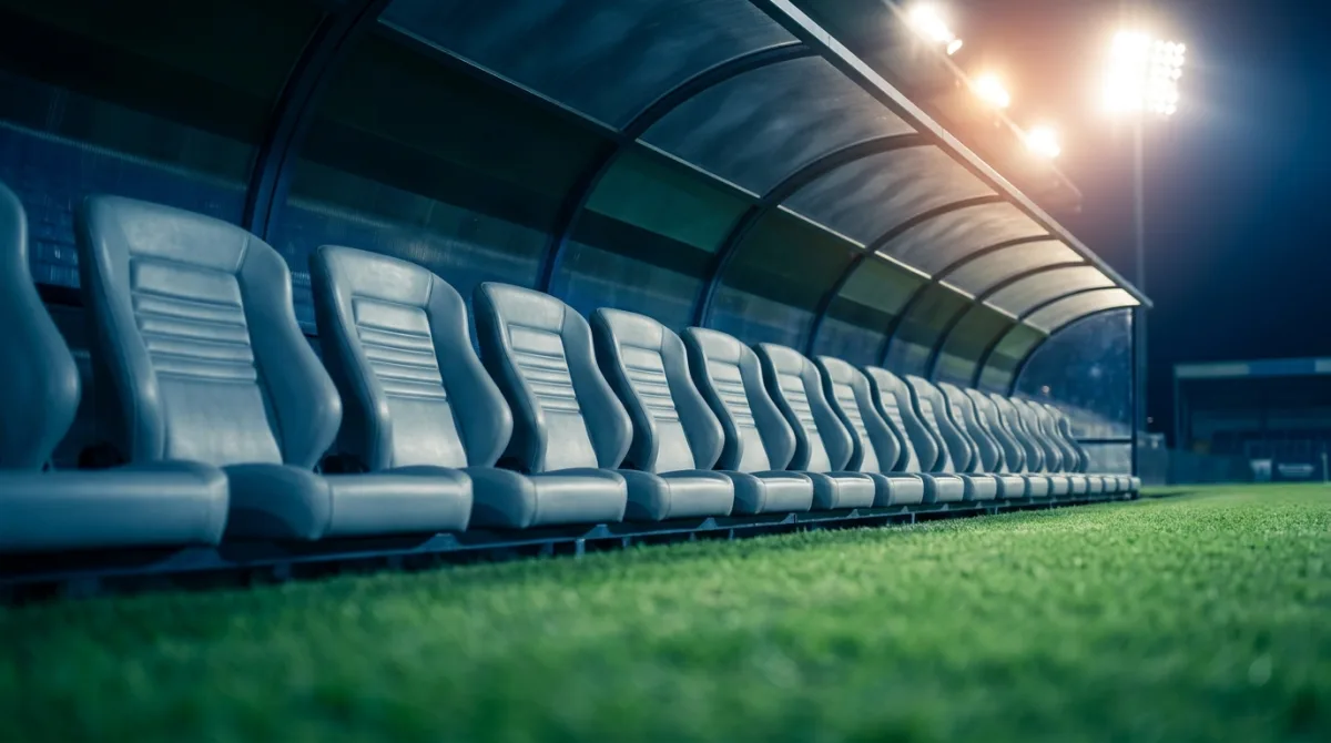 An empty row of dugout seats beside a floodlit football pitch at night