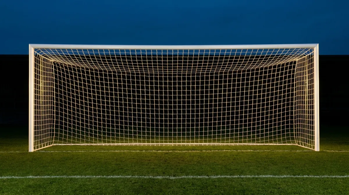 An empty floodlit football goal and net photographed straight on at dusk