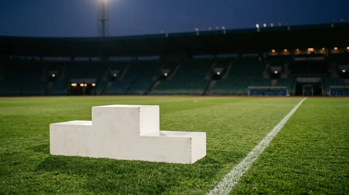 An empty three-step medal presentation podium on a floodlit football pitch at dusk