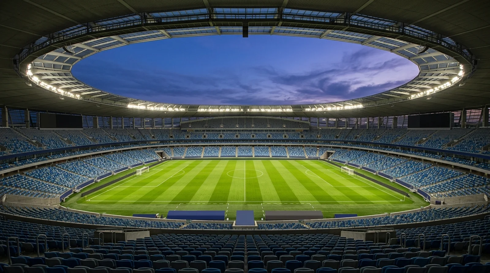 An empty floodlit football stadium at dusk with the pitch mown in stripes
