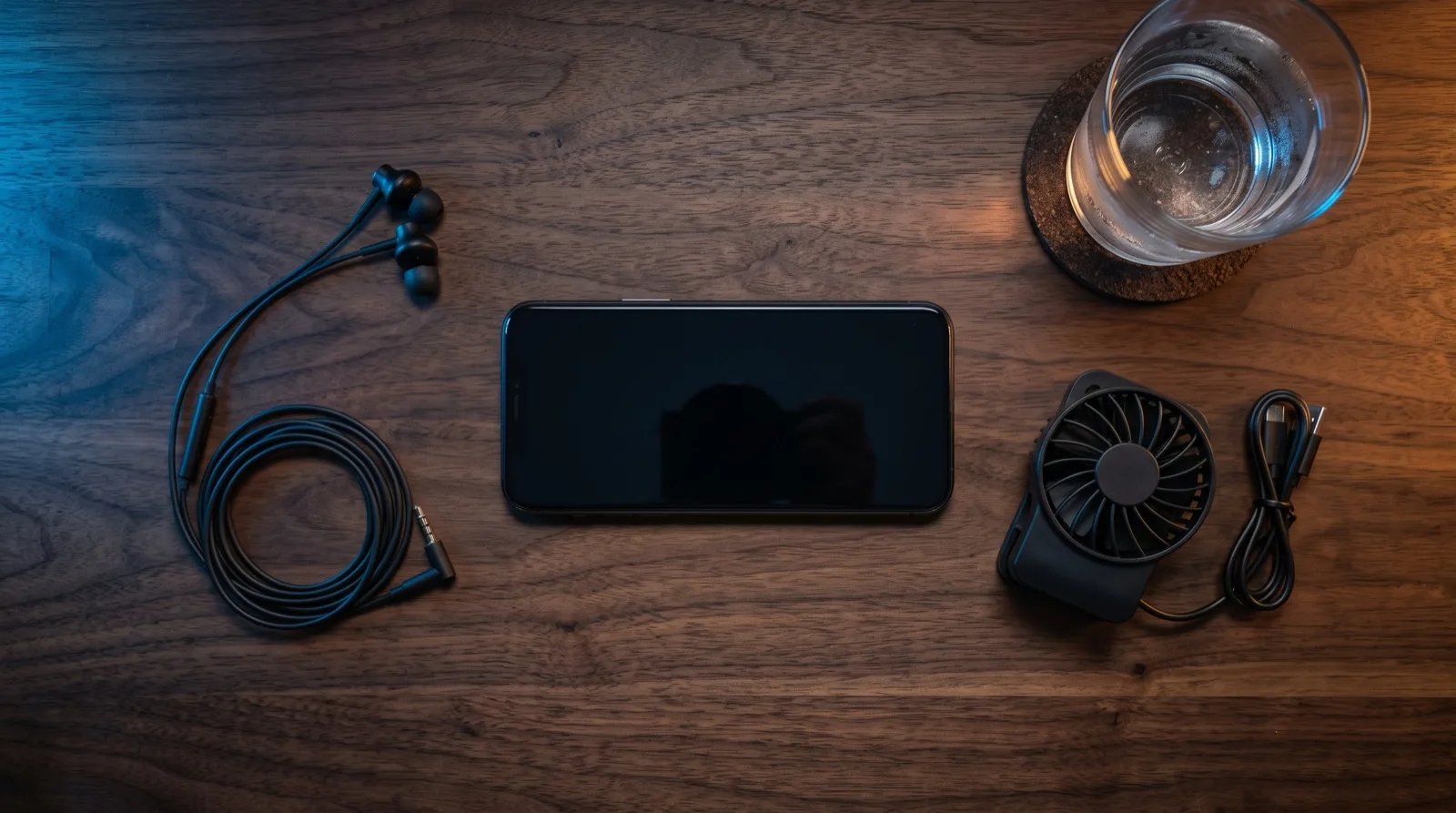 Overhead view of a mobile gaming setup with a phone, clip-on cooling fan and earphones on a desk