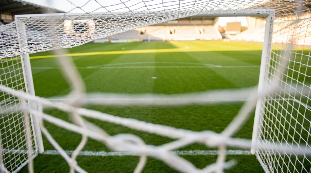 The view out from inside a goal, netting in the foreground and an empty penalty area beyond