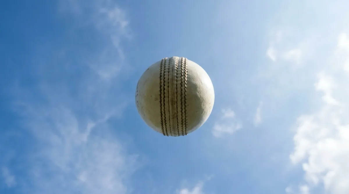 A white cricket ball high in the air against a blue sky
