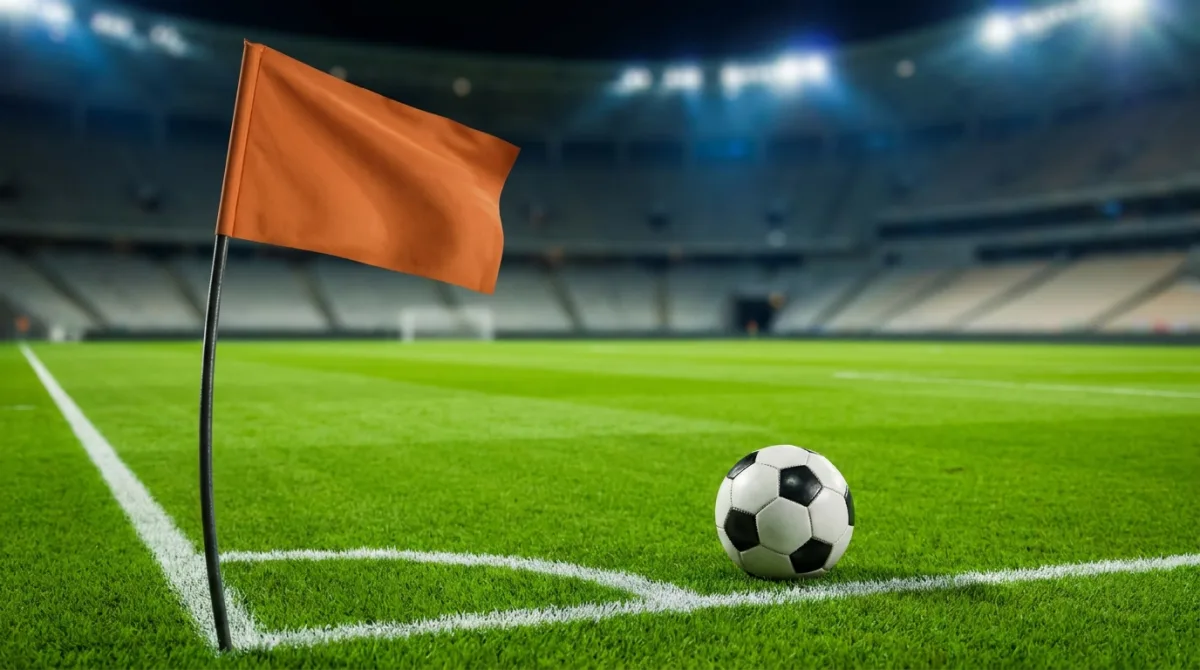 A corner flag and a match ball at the corner of a floodlit stadium pitch
