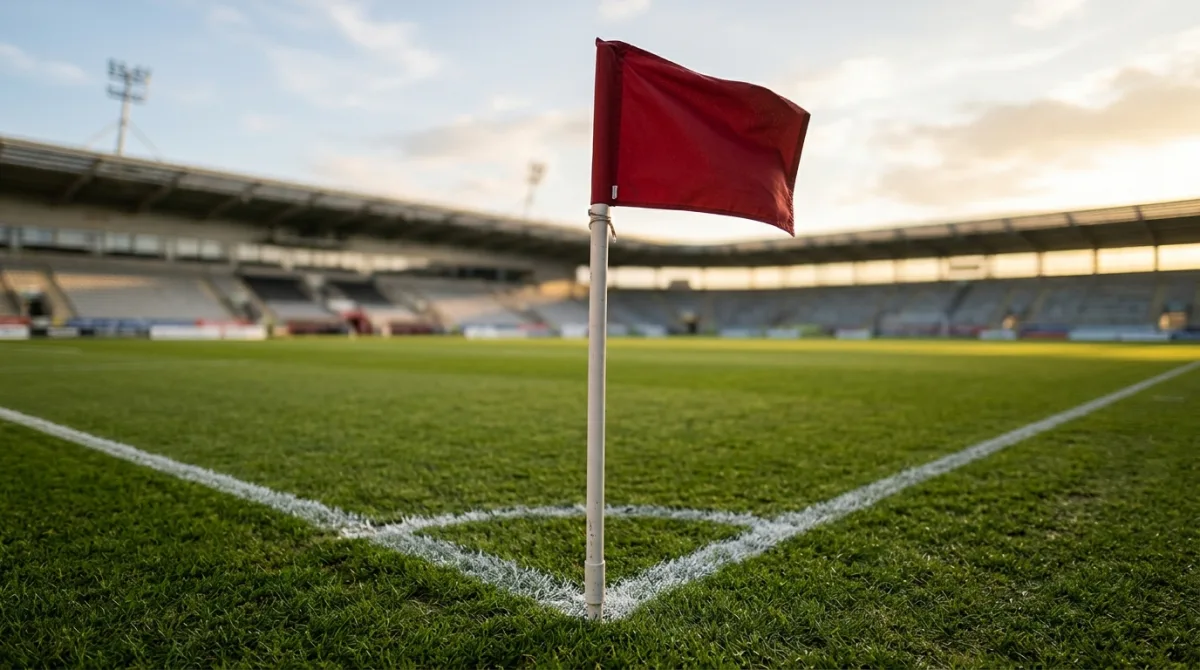A red corner flag standing where two painted white lines meet at the corner of a stadium pitch