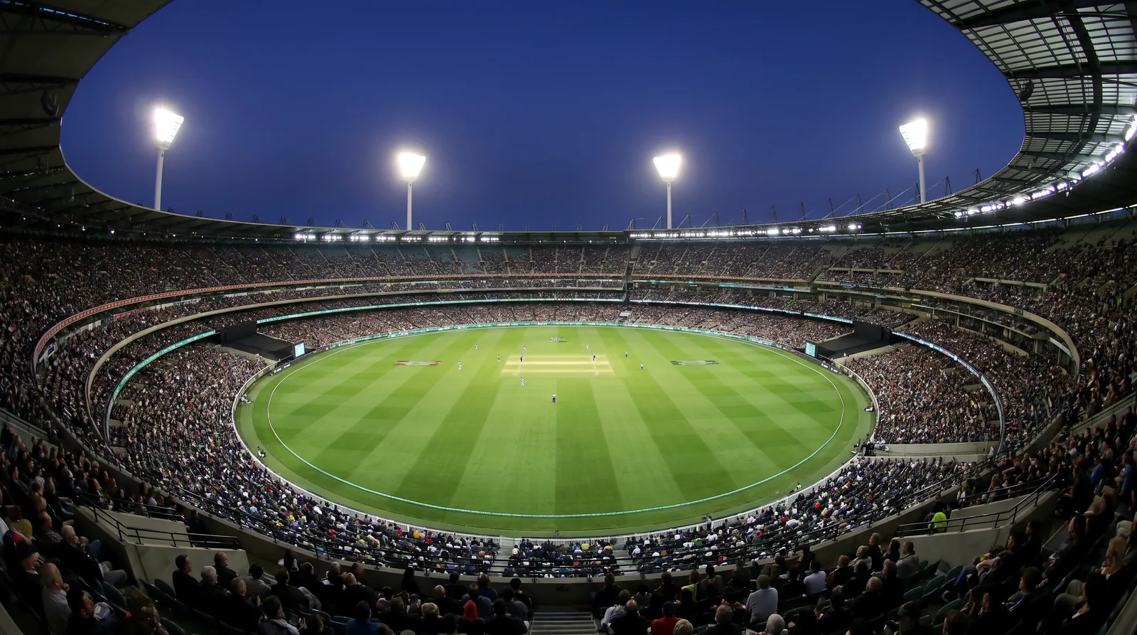 A packed floodlit cricket stadium seen from high in the stands during a night match