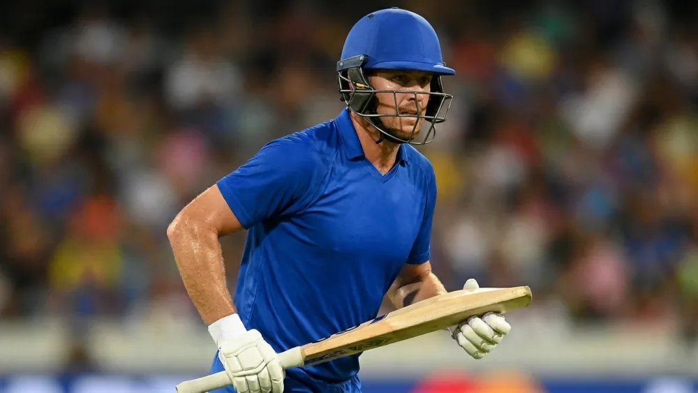 A batsman in plain blue kit running hard between the wickets under floodlights