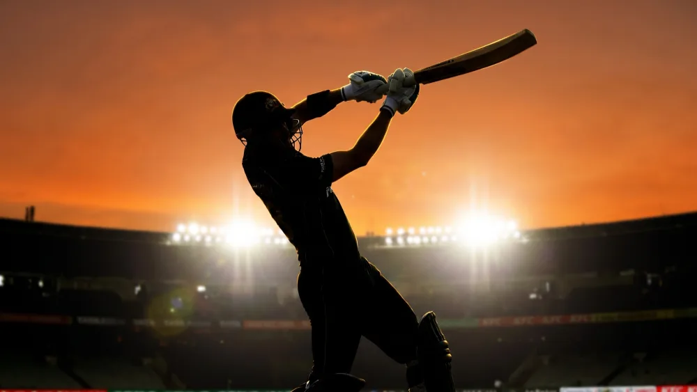 A batsman silhouetted against a sunset sky as he follows through on a lofted shot over the stadium floodlights