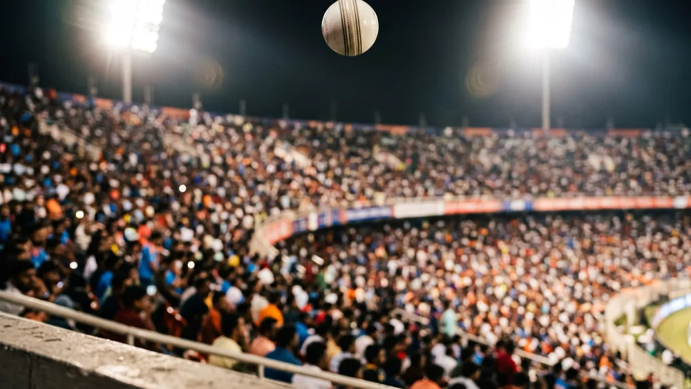 A white cricket ball sails towards a packed floodlit stand at a night T20 match