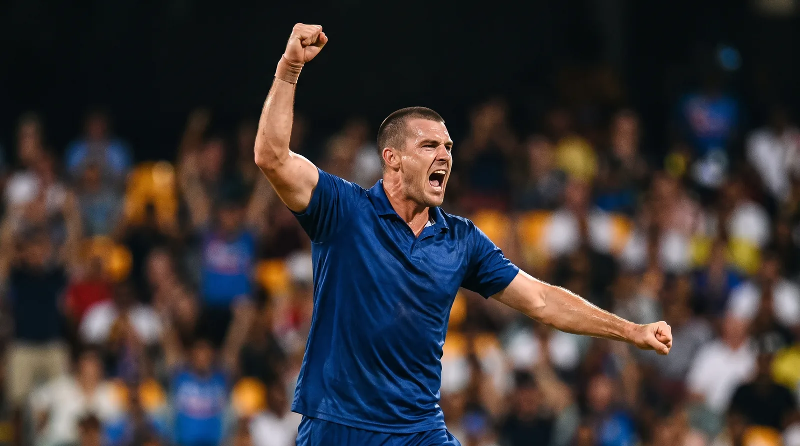 A fast bowler in blue celebrates taking a wicket under floodlights