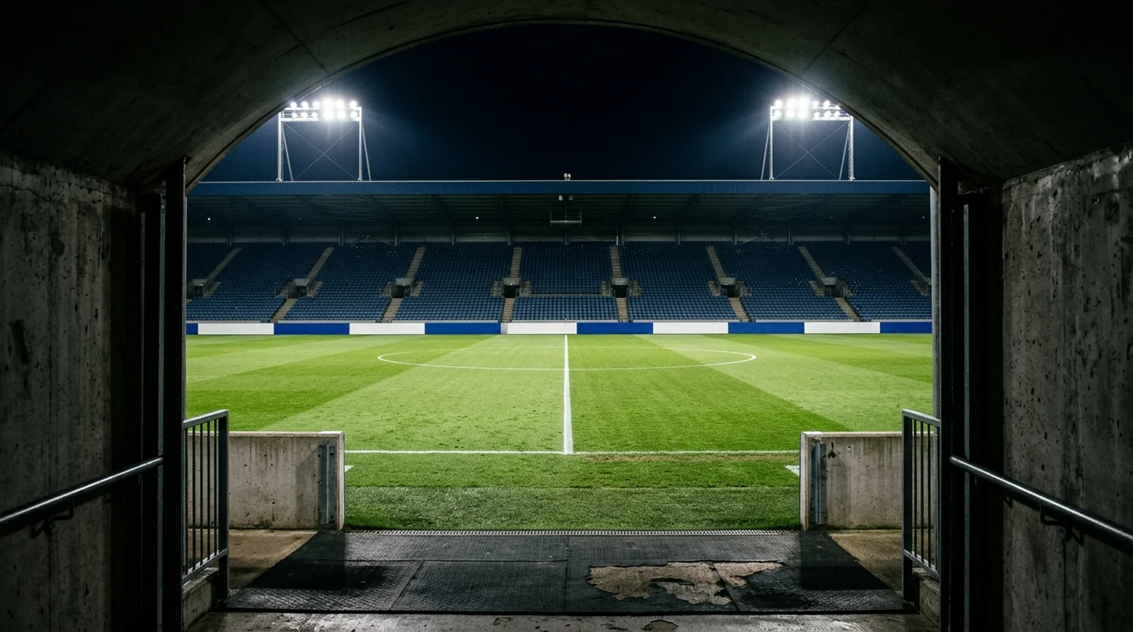 The view from a stadium players tunnel out to the halfway line of an empty floodlit pitch