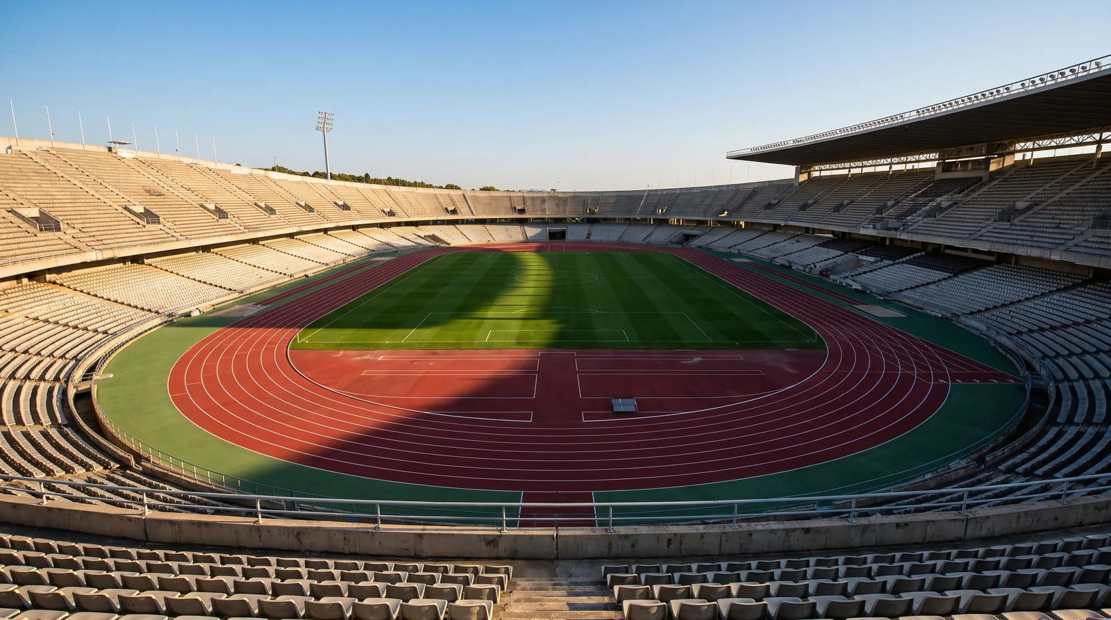 An empty Olympic athletics stadium with a red running track encircling a green football pitch