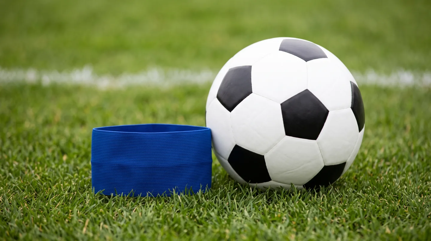 A plain blue captain's armband lying on green grass beside a football