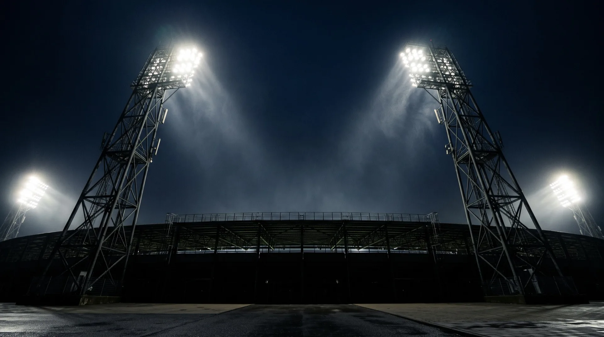 Stadium floodlight pylons blazing against a dark night sky above a silhouetted stand