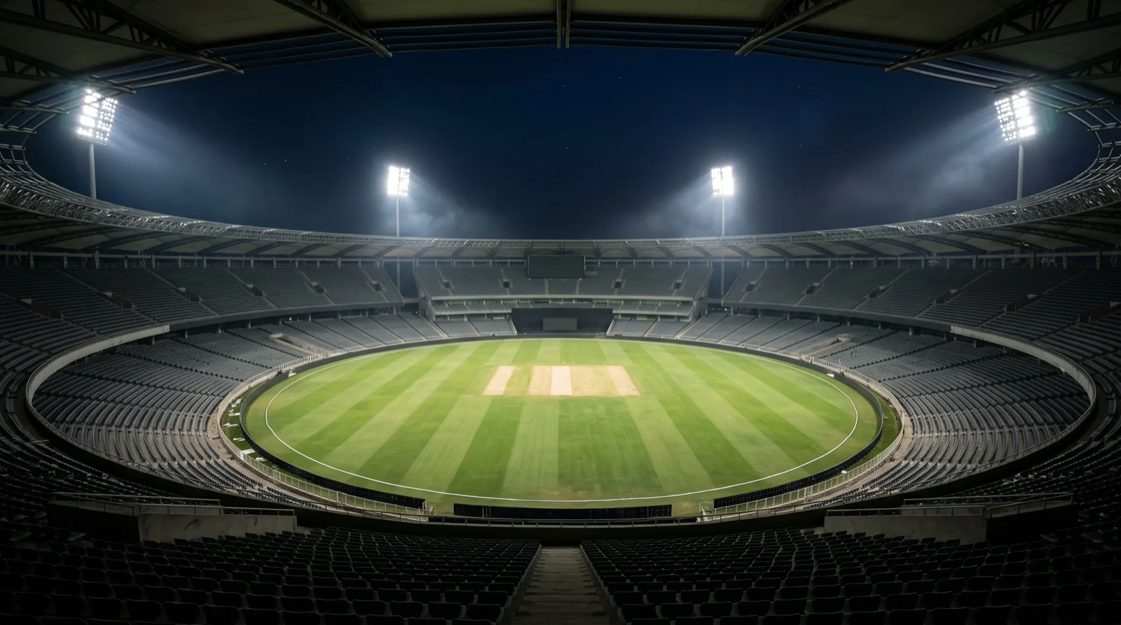 An empty floodlit cricket stadium at night with the pitch strip at the centre of the oval