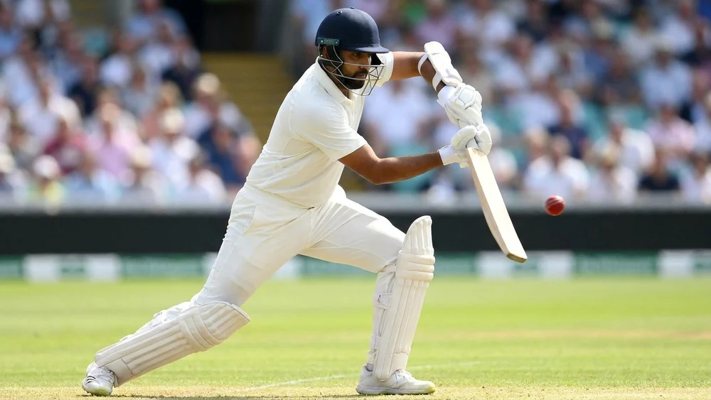 A batsman in Test whites drives at a red ball in daylight