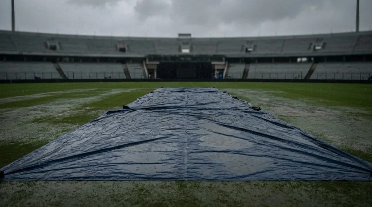 Rain covers pulled across the pitch at an empty cricket ground during a downpour