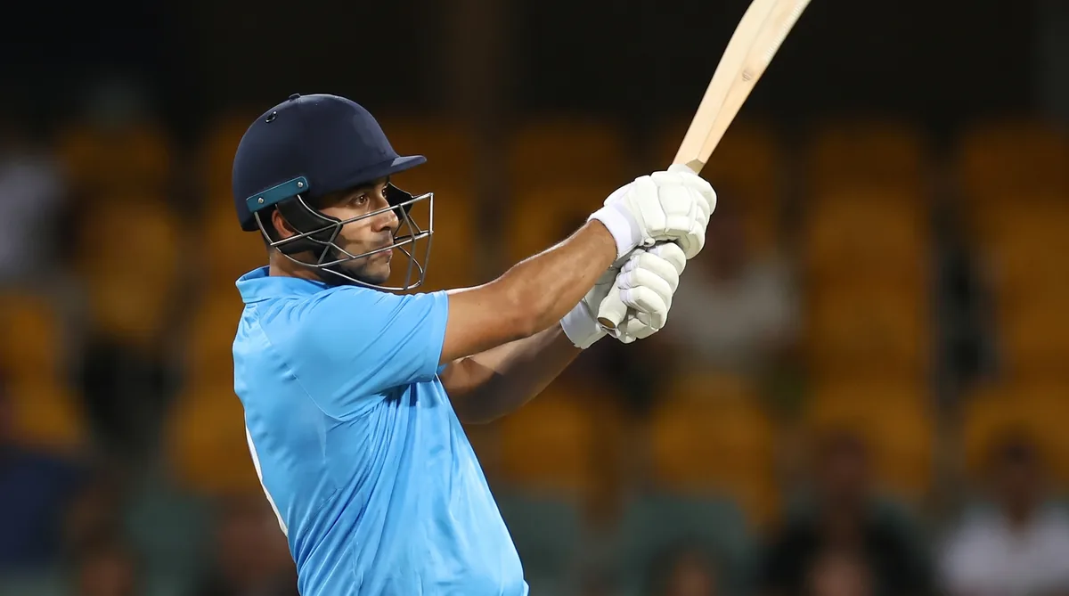A batter in light blue limited-overs kit plays a drive under floodlights