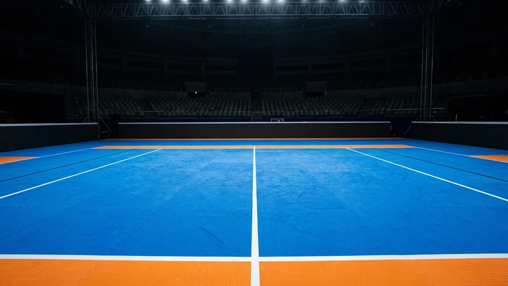 An empty blue and orange kabaddi mat under arena spotlights in a darkened indoor stadium