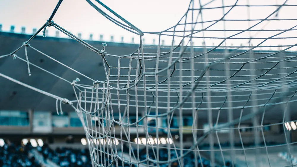 Close-up of a football goal net with the stands of a stadium blurred behind it