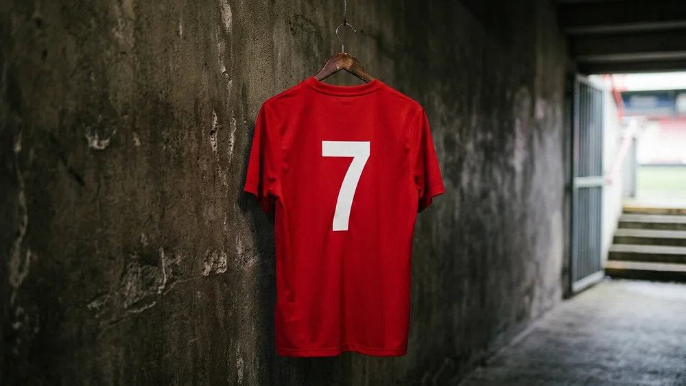 A plain red football shirt with a white number 7 on the back, hanging in a stadium tunnel